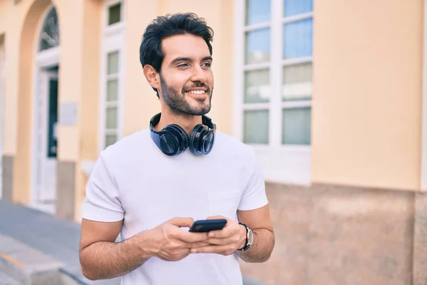 Young hispanic man smiling happy using smartphone and headphones at city.