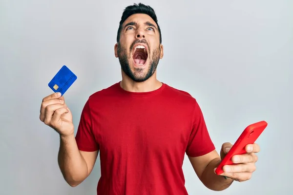 Joven Hispano Sosteniendo Teléfono Inteligente Tarjeta Crédito Enojado Loco Gritando —  Fotos de Stock