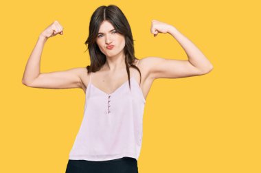 Genç, güzel, beyaz bir kız. Sıradan kıyafetler giyiyor. Kollarında gururla gülümseyen kaslar var. fitness konsepti. 