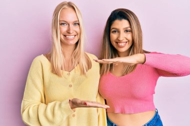 İki arkadaş pembe arka planda el kol hareketleri yaparak büyük ve büyük boy işareti gösteriyorlar. Ölçüm sembolü. Kameraya bakıp gülümsüyor. ölçüm kavramı. 