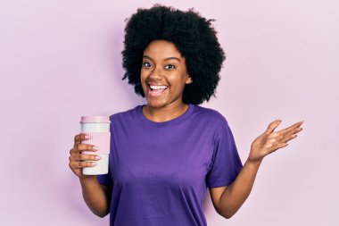 Genç Afro-Amerikalı kadın kahveyi mutlu bir gülümsemeyle kutluyor ve kazanan el kaldırarak ifade ediyor. 