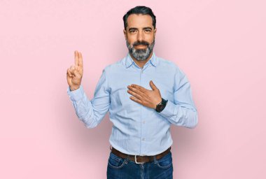 Orta yaşlı, sakallı, iş gömleği giyen, gülümseyen, elleri göğsünde ve parmakları havada küfür eden sadakat yemini eden bir adam. 