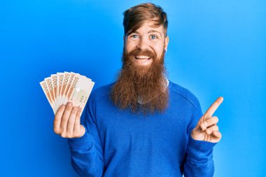 Genç İrlandalı kızıl saçlı adam elinde 5000 Güney Koreli para kazandı gülümseyerek mutlu bir şekilde elini ve parmağını kenarda gösterdi. 