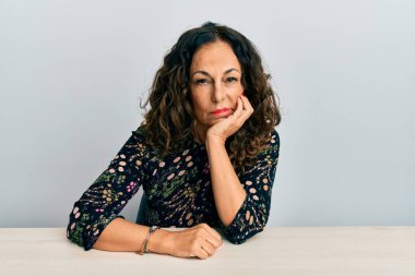 Masada oturan orta yaşlı güzel bir kadın kollarını kavuşturup depresyondan sıkılmış ve yorgun görünüyor.. 