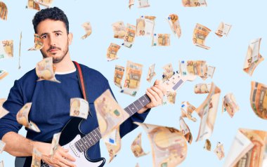 Genç İspanyol adam elektro gitar çalıyor. Düşünme tarzı ve ayık yüz ifadesi. Kendine güveniyor gibi görünüyor.