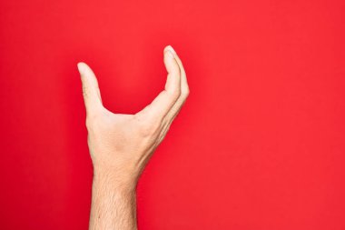 Kafkasyalı genç adam parmaklarını izole edilmiş kırmızı arka plan üzerinde gösteriyor ve görünmez şeyi alıyor, parmakları boşluk gösteren nesneleri tutuyor.