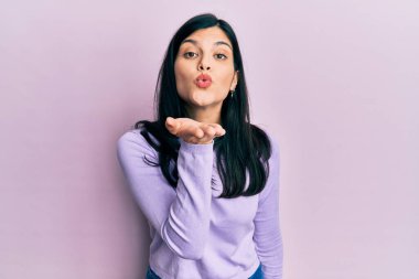 Gündelik giysiler giymiş genç İspanyol bir kadın kameraya bakıp havada bir öpücük savuruyor ve sevimli ve seksi oluyor. aşk ifadesi. 