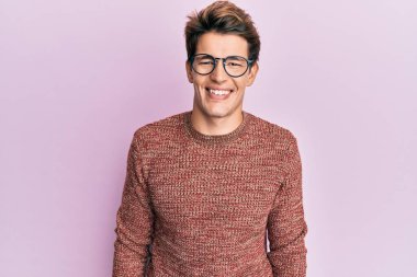 Yakışıklı, beyaz bir adam günlük süveter giyiyor ve yüzünde mutlu ve havalı bir gülümsemeyle gözlük takıyor. şanslı kişi. 