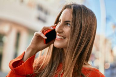 Genç İspanyol kadın gülümsüyor. Şehirdeki akıllı telefondan konuşuyor..