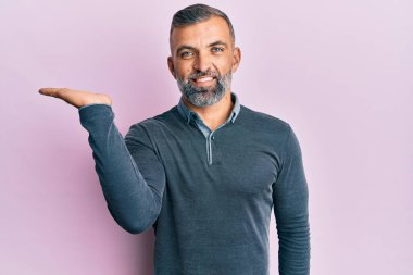 Orta yaşlı, sıradan kıyafetler giyen, neşeli bir şekilde gülümseyen, avuç içi kameraya bakan yakışıklı bir adam.. 