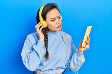 Akıllı telefon ve kulaklık kullanan genç İspanyol kız yüzünde ciddi bir ifadeyle rahatladı. Basit ve doğal bir şekilde kameraya bakıyorsun.. 