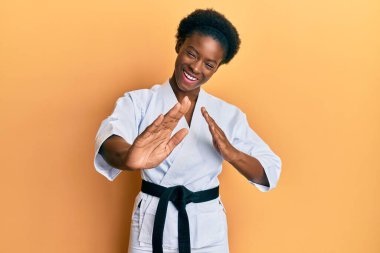 Young african american girl wearing karate kimono and black belt smiling and laughing hard out loud because funny crazy joke. 