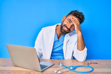 Klinikte çalışan, doktor üniforması giyen genç İspanyol bir adam. Elleri havada, şaşırmış ve sinirli bir halde. 