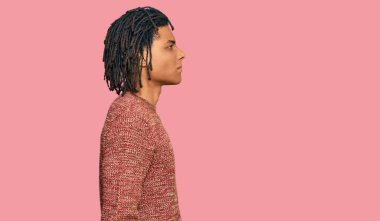 Afro-Amerikalı genç bir adam günlük kışlık süveter giyiyor. Taraf arıyor, rahat bir poz veriyor. Kendine güvenen bir gülümsemesi var.. 