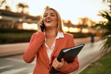 Genç sarışın iş kadını gülümsüyor. Şehirdeki akıllı telefondan konuşuyor..