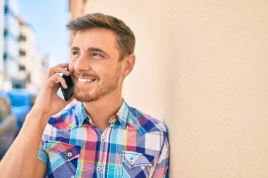 Genç beyaz adam gülümsüyor. Şehirdeki akıllı telefondan konuşuyor..