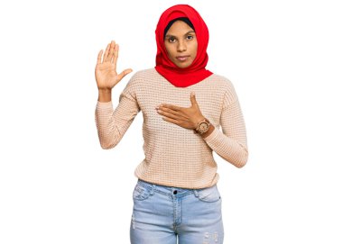 Young african american woman wearing traditional islamic hijab scarf swearing with hand on chest and open palm, making a loyalty promise oath  clipart
