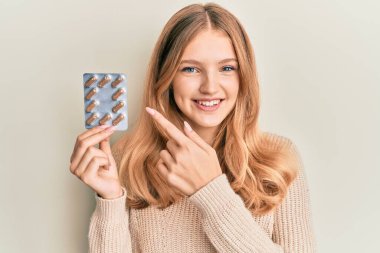 Güzel, genç, beyaz bir kız elinde haplarla gülümsüyor. 