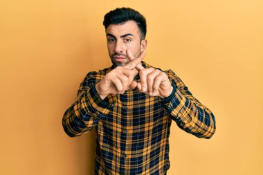 Gündelik kıyafetler giyen genç İspanyol adam reddedilme ifadesini negatif işaret yaparak parmaklarını çapraz yapıyor. 
