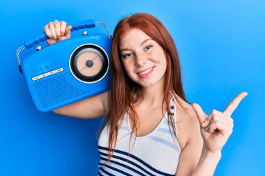 Genç kızıl saçlı kız elinde klasik bir radyo tutarken gülümsüyor mutlu bir şekilde elini ve parmağını yana uzatıyordu. 