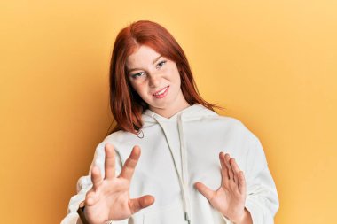 Genç, kızıl saçlı, sıradan bir kazak giyen, tiksindirici bir yüz ifadesi takınan, tiksindirici bir yüz ifadesi takınan, tiksindirici bir yüz ifadesi olan bir kız. Eller havada. 