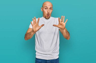 Sakallı, günlük beyaz tişörtlü, korku ifadesinden korkmuş ve dehşete düşmüş kel bir adam. El kol hareketi yapmayı kes, şok içinde bağır. panik konsepti. 