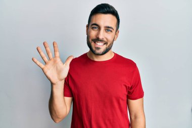 Gündelik kıyafetler giyen genç İspanyol adam beş numarayı gösterip işaret ederken kendinden emin ve mutlu bir şekilde gülümsüyor.. 