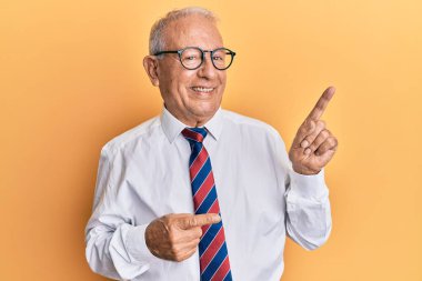 İş kıyafetleri giymiş, gülümseyen ve kameraya bakan beyaz bir adam. İki eli ve parmakları yanda.. 