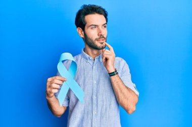 Mavi kurdeleli genç bir adam ciddi bir yüzle eli çenesinde soru sormayı düşünüyor, kafa karıştırıcı bir fikir. 