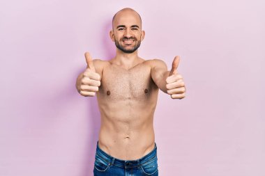 Tişörtsüz genç bir adam elinde olumlu bir jest yapmayı onaylıyor. Gülümsüyor ve başarı için seviniyor. kazanan jest. 