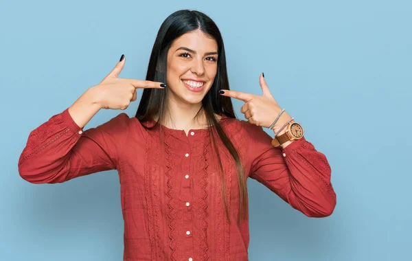 若いヒスパニック系の女性は陽気な笑みを浮かべてカジュアルな服を着て指の歯と口を指しています 歯の健康の概念 — ストック写真