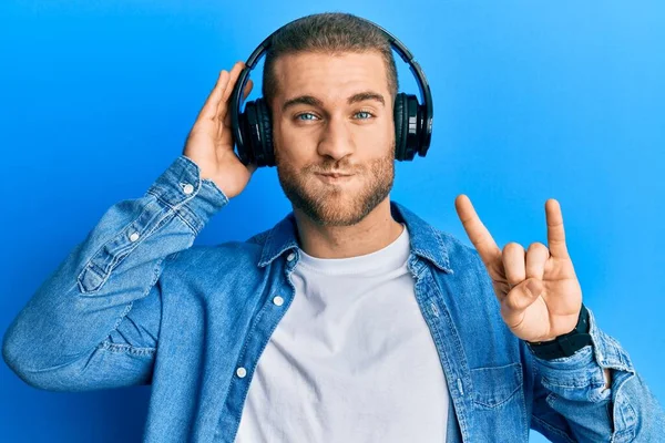 Young Caucasian Man Using Headphones Doing Rock Symbol Puffing Cheeks — Stock Photo, Image