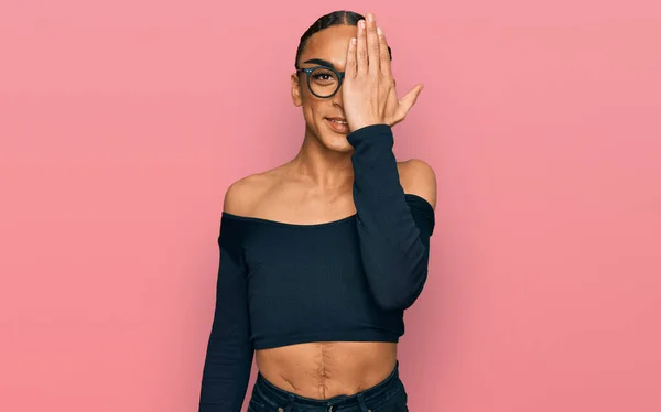 Hispanic transgender man wearing make up and long hair wearing women clothes covering one eye with hand, confident smile on face and surprise emotion.