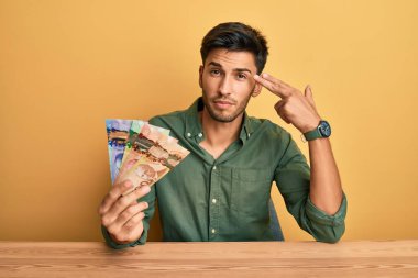 Genç yakışıklı adam Kanada doları tutuyor. Kendini vuruyor ve öldürüyor. Elini ve parmaklarını silah gibi kullanıyor.. 