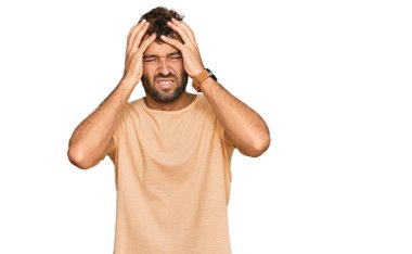 Sakallı, sıradan tişörtlü, baş ağrısı çeken, çaresiz ve stresli genç bir adam. Çünkü acı ve migren ağrısı var. Eller başının üstünde.. 