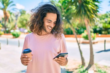 Genç İspanyol adam mutlu bir şekilde gülümsüyor. Akıllı telefon kullanıyor ve şehirde kahve içiyor..