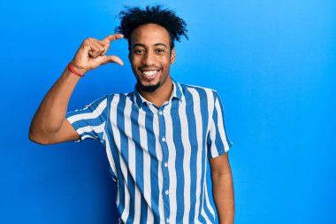 Sakallı, sıradan çizgili tişörtlü, gülümseyen, kendine güvenen, el hareketi yapan, parmaklarıyla işaret yapan ve kameraya bakan Afro-Amerikan genç bir adam. ölçüm kavramı. 