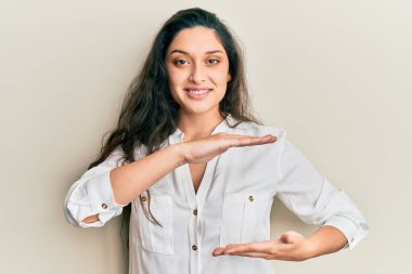 Güzel bir ortadoğulu kadın, sıradan kıyafetler giyip, büyük ve büyük boylarda işaretler göstererek el kol hareketi yapıyor. Kameraya bakıp gülümsüyor. ölçüm kavramı. 