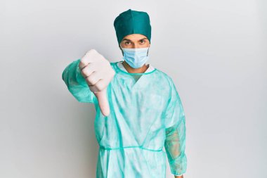 Cerrah üniforması ve tıbbi maske takan genç yakışıklı adam mutsuz ve kızgın görünüyor. Reddedilmiş ve olumsuz bir hareket sergiliyor. kötü ifade. 