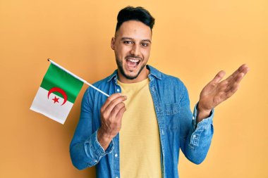 Cezayir bayrağını tutan genç Arap adam başarıyı mutlu bir gülümsemeyle ve kazanan yüz ifadesiyle kutluyor. 