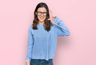 Genç ve güzel bir kadın günlük kıyafetler ve gözlük takıyor gülümsüyor ve kendinden emin bir şekilde el hareketi yapıyor parmaklarıyla işaret yapıyor ve kameraya bakıyor. ölçüm kavramı. 