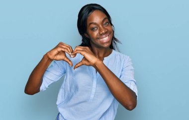 Genç Afro-Amerikan kadın gündelik giysiler giyiyor. Aşık gülümsüyor. Elleriyle kalp sembolü ve şekli gösteriyor. romantik kavram. 