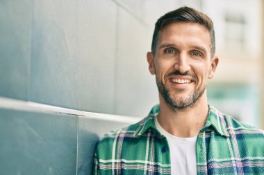 Genç beyaz adam gülümseyerek şehirde mutlu mesut duruyor..