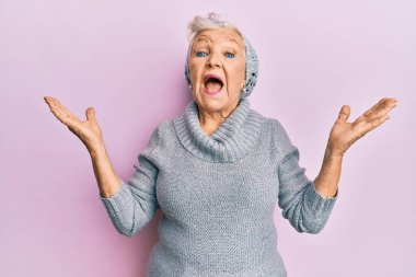 Kıdemli gri saçlı kadın yün kazak ve kış şapkası giyip zaferi mutlu bir gülümsemeyle ve kazanan ifadeyle kutluyor. 