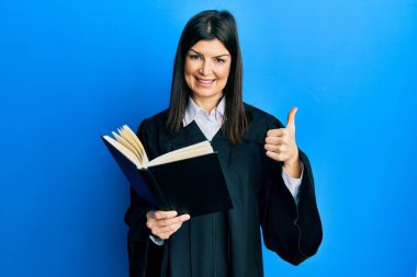 Genç İspanyol kadın yargıç üniforması giyiyor mutlu ve pozitif gülümsüyor, başparmağıyla mükemmel ve onay işareti yapıyor. 