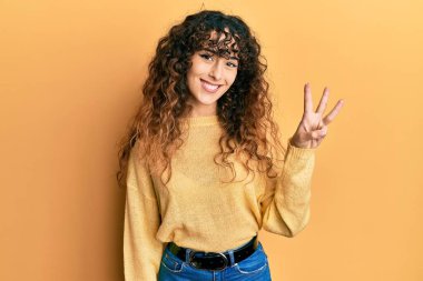 Gündelik kıyafetler giyen genç İspanyol kız üç numarayı gösterip işaret ederken kendinden emin ve mutlu bir şekilde gülümsüyor.. 