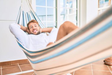 Yakışıklı beyaz adam mutlu bir şekilde gülerek terasta dinleniyor.