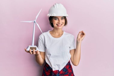 Mimar kasketli genç beyaz kadın elinde yel değirmeniyle mutlu bir şekilde gülümsüyor. 