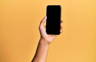İzole edilmiş sarı arka planda akıllı telefon gösteren İspanyol bir adamın eli..