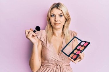 Makyaj fırçası ve allık palet tutan beyaz bir kadın. Hiçbir şeyden haberi yok ve kafası karışık. şüphe kavramı. 